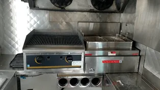 A charbroiler and a fryer installed on a stainless line inside a food truck